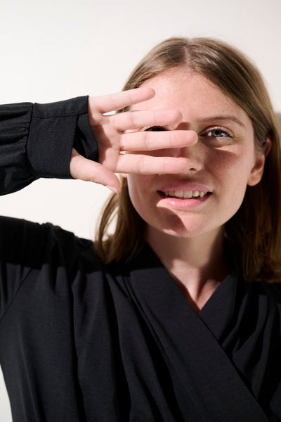 Femme souriante portant un shrug anti-UV noir UPF 50+, protection solaire élégante et confortable.