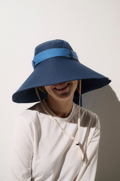 Femme portant un chapeau anti-UV bleu à bord large, offrant une protection solaire élégante et confortable.