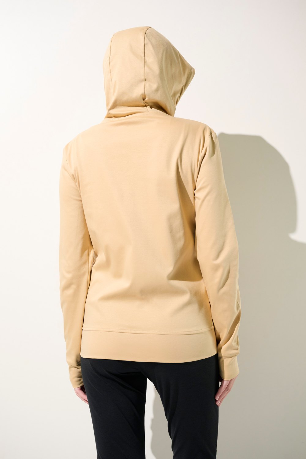Femme vue de dos portant une veste anti-UV à capuche de couleur beige. Idéale pour se protéger du soleil dans toutes ses activités quotidiennes.