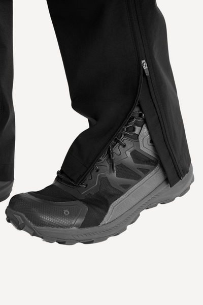 Pantalon anti-UV noir avec fermeture éclair, porté avec des chaussures de randonnée robustes pour activités en extérieur.