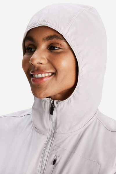 Femme sourire portant une veste anti-UV blanche à capuche, légère et respirante, offrant protection UPF 50+.