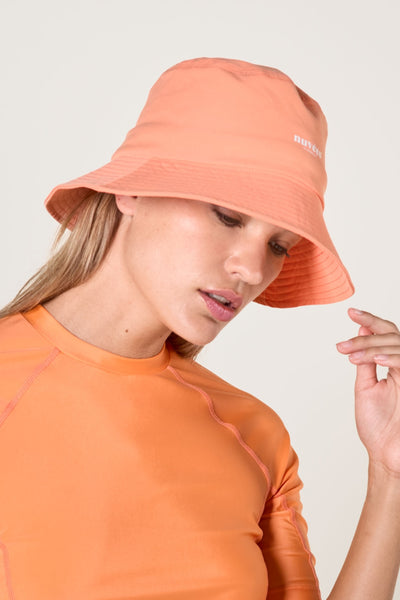 Femme portant un bob anti-UV couleur saumon, idéal pour se protéger des UV au quotidien.